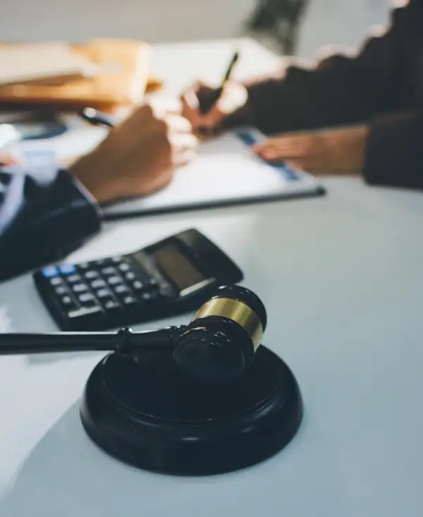 Gros plan sur un bureau avec les mains de 2 personnes face à face. Au premier plan, un marteau de juge puis en arrière plan une calculatrice et des dossiers