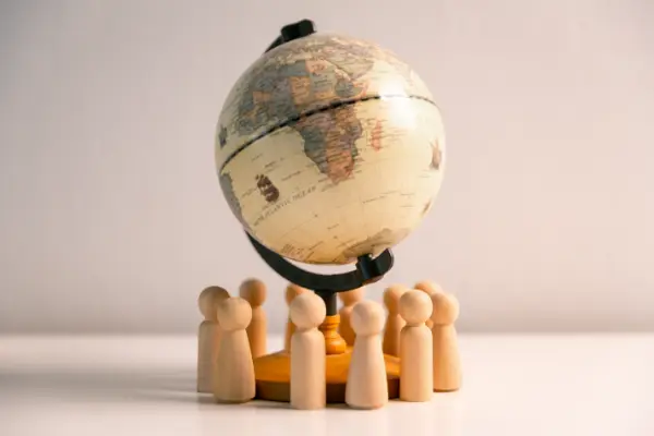 Photo en plan serré de petits personnages en bois symbolisant des expatriés au pied d'un globe